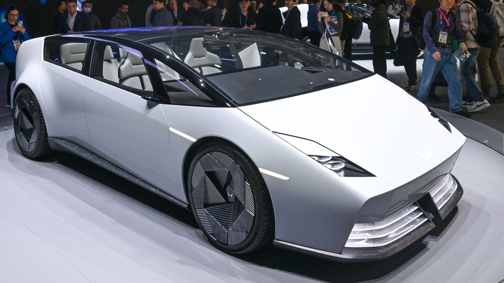 A sleek white honda ev on a platform at a trade show, with people taking pictures