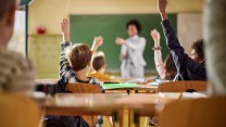 Rear view of school kids raising their hands to answer the teacher's question on a class at elementary school.