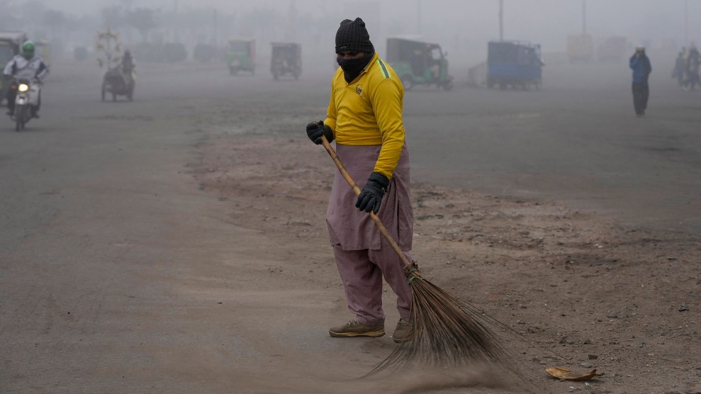 Man wearing mask sweeping a street amid heavy air pollution.