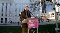 A man stands on a podium with a pink sign attached to it that reads, "60,000 voters won't be silenced."