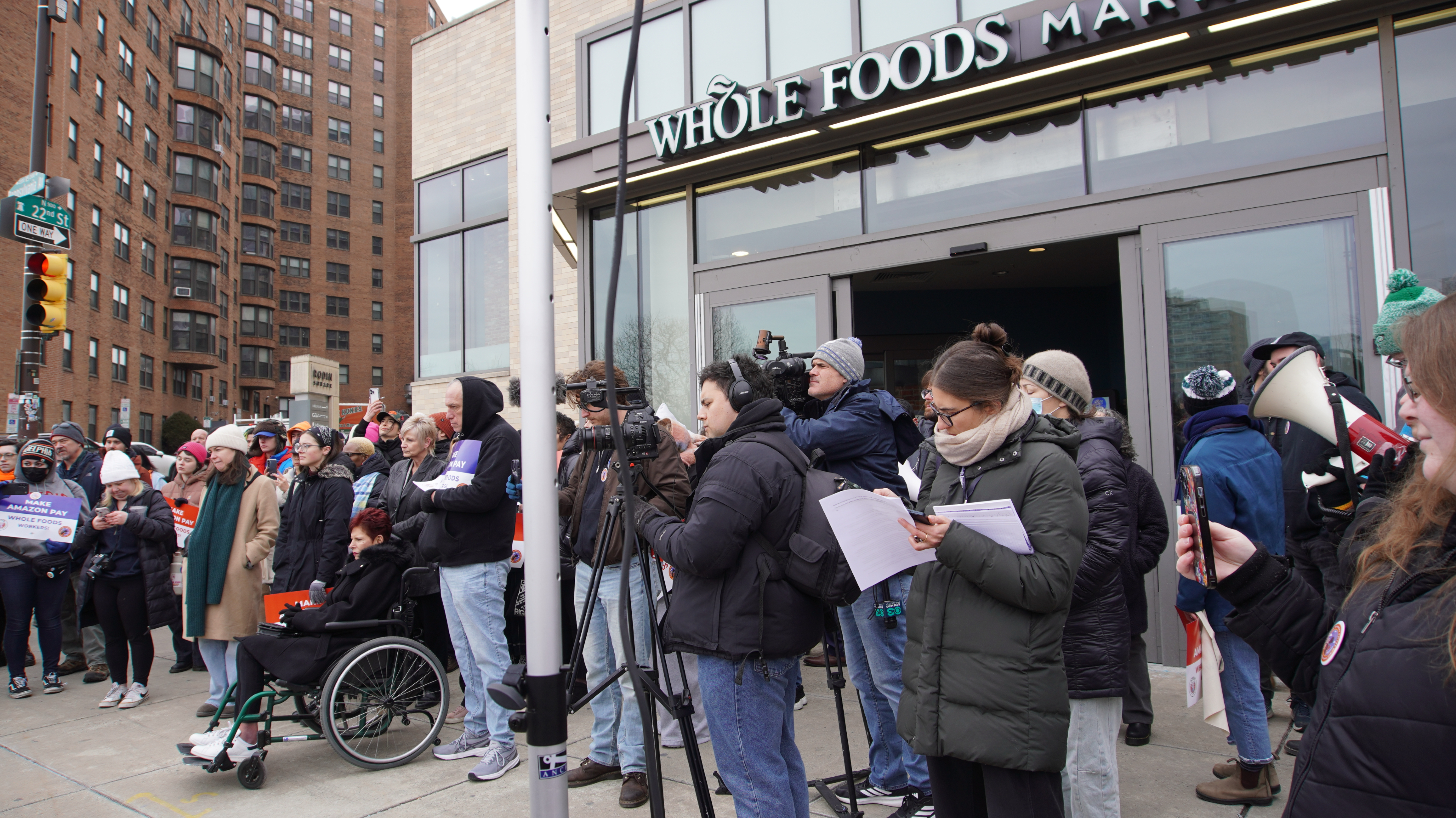 Dozens of people stand in front of an entrance to the Whole Foods store.