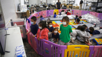 Over 15 young unaccompanied migrants, from ages 3 to 9, watch television inside a playpen at the U.S. Customs and Border Protection facility in Donna, Texas. One woman is outside with a child and staff is walking around