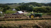 A green tractor in a field in front of rolling hills.