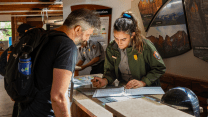 A hiker and a park ranger lean over a table, looking at a folder.