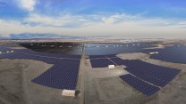 Solar panels spread over a landscape in front of a big blue sky.