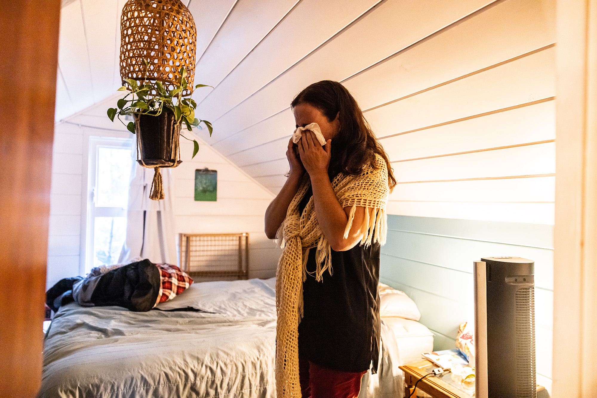 Woman with her face in her hands, standing in a bedroom.