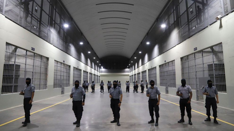Six uniformed men stand in a row in a wide hallway between holding cells.