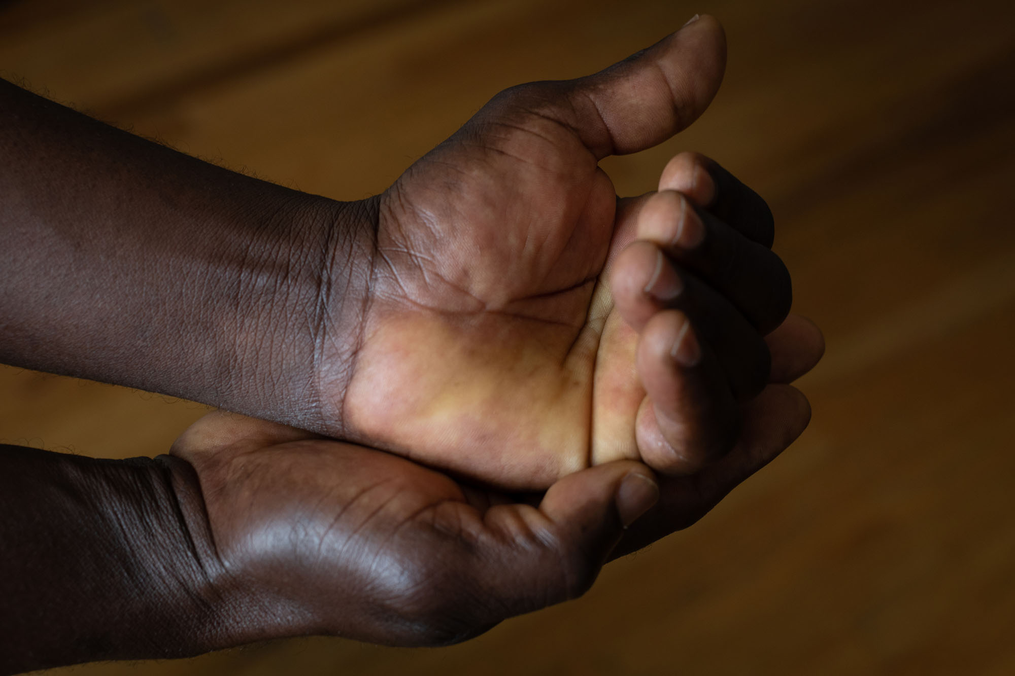 Close-up of a man's hands. He holds his left hand palm up in his right; the fingers of his left hand are partially curled shut.