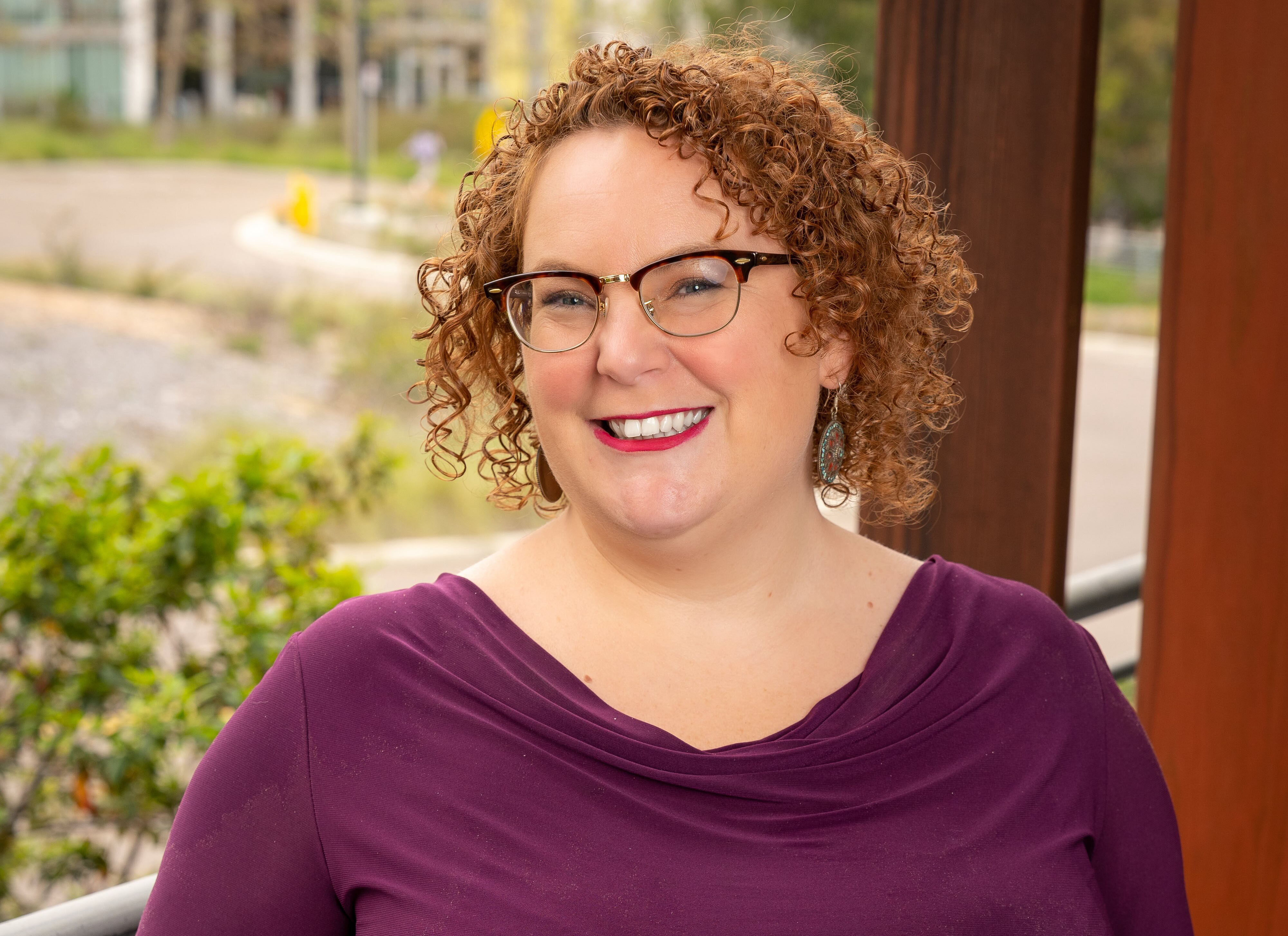 Headshot of smiling bespectacled woman with a bob and tight curls.