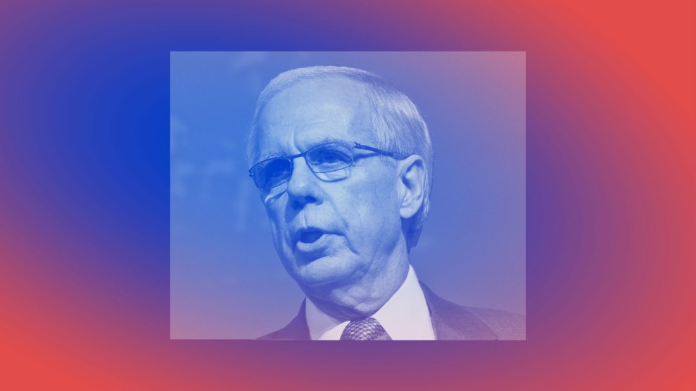A silver-haired white male with glasses wearing a suit. His square pictured is centered over a horizontally rectangular shape. The entire image is bathed in a red and blue gradient.