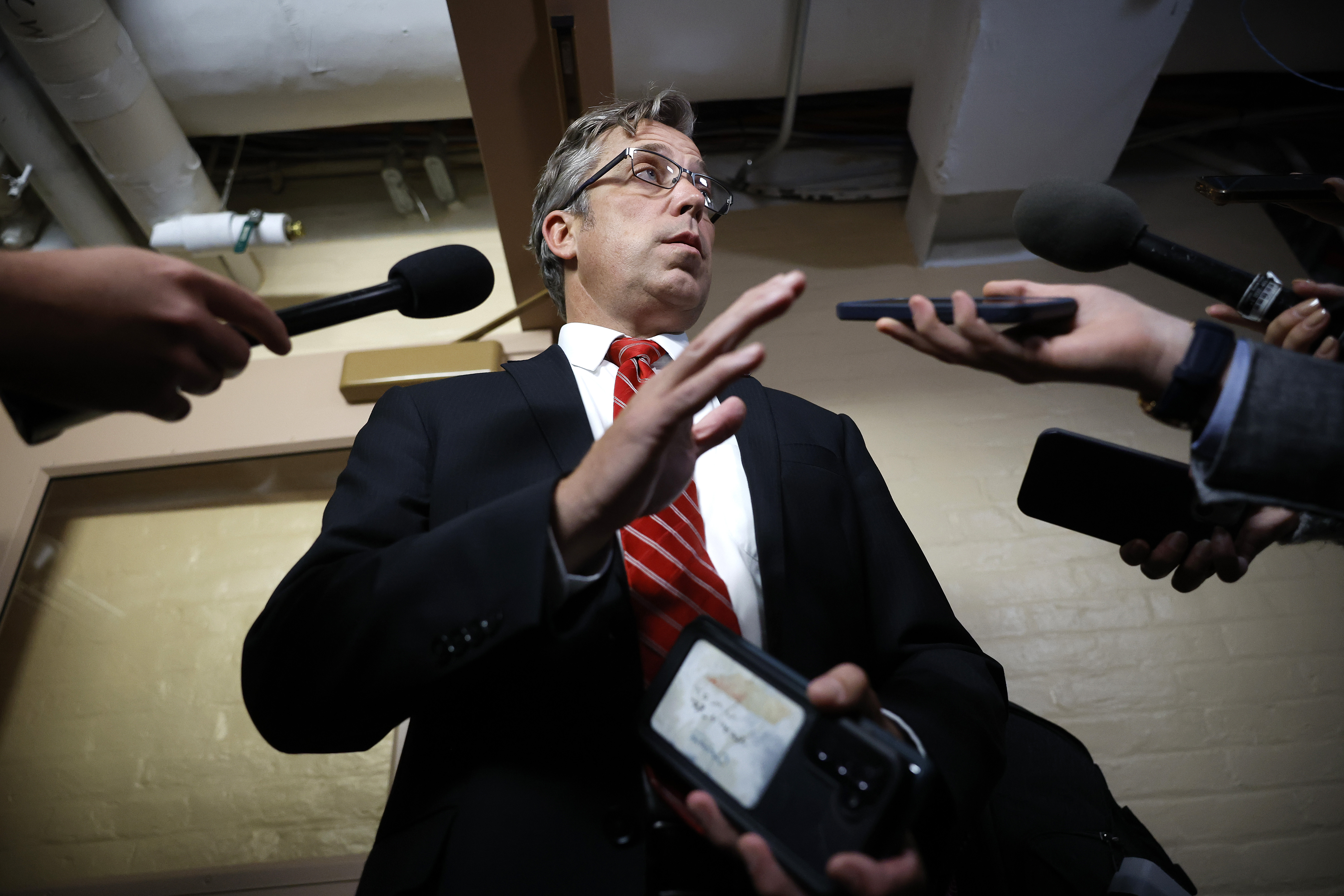 Andy Ogles is shown from below, with several people holding microphones and smartphones near his face.