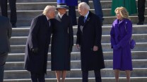 Three people wearing black jackets and one person wearing a blue jacket stand together in front of stairs.