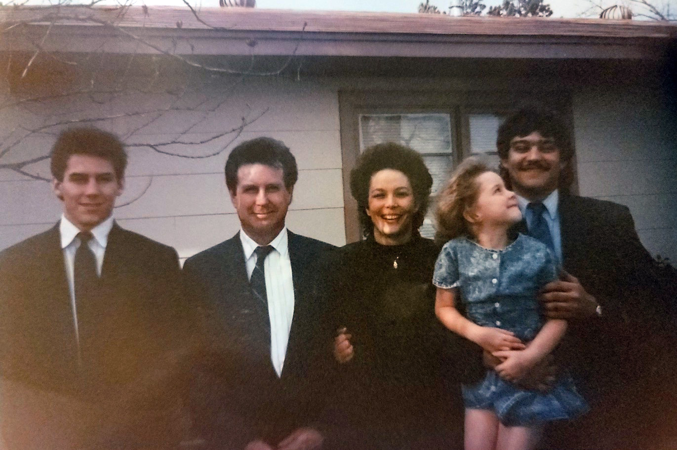 Group of four adults and one child smiling, standing outside.