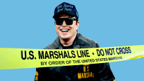 A photo illustration of Elon Musk, a middle-aged Caucasian man, smiling with mouth agape, teeth visible. He's wearing sunglasses, a black baseball cap with the words "Make America Great Again" in gothic type. He's illustrated wearing a black jacket with U.S. Marshal written on the left breast in gold. The circular logo of the orgnization with a star at the center is above the words. And, seemingly in front of Musk is a string of yellow tape that reads in black sans serif type: "U.S. Marshals Line ... Do not cross ... By order of the United States Marshal."