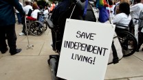A sign on a behind someone in a wheelchair that says, "Save Independent Living"