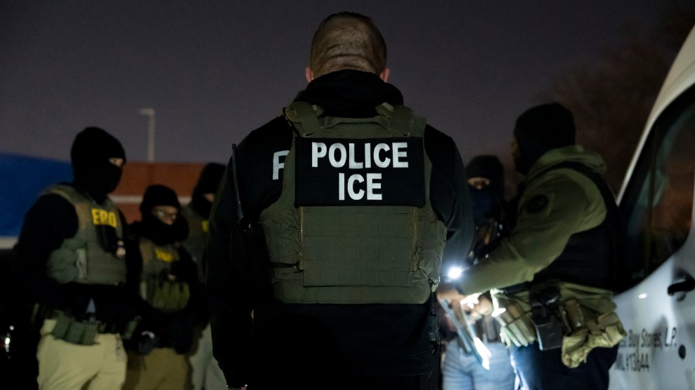 A group of ICE agents gathered in a circle, with the back of the uniform saying "Police Ice" being the most visible. It is evening in the photo