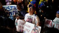 A woman cries while holding a sign printed with family photos that says "Jhon William Chacin Gomez" in the center.