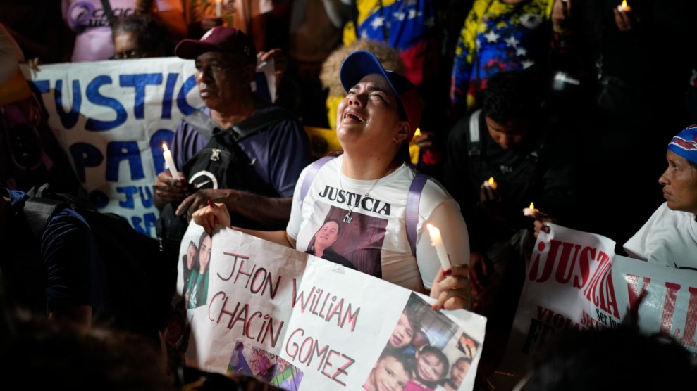 A woman cries while holding a sign printed with family photos that says "Jhon William Chacin Gomez" in the center.