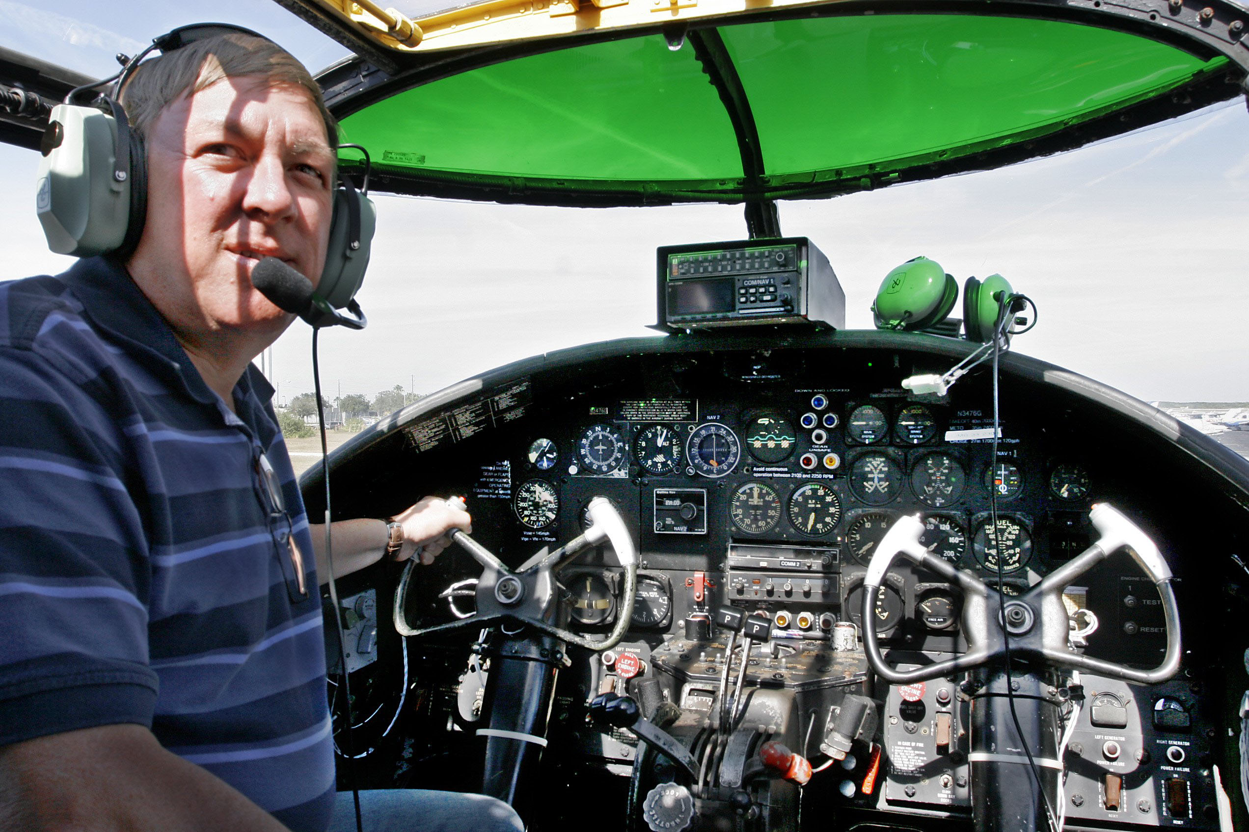 Man with headset sits in the cockpit of a warplane.