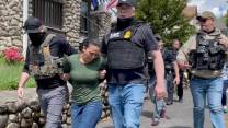 An immigrant wearing a green shirt is led away by two ICE officers.