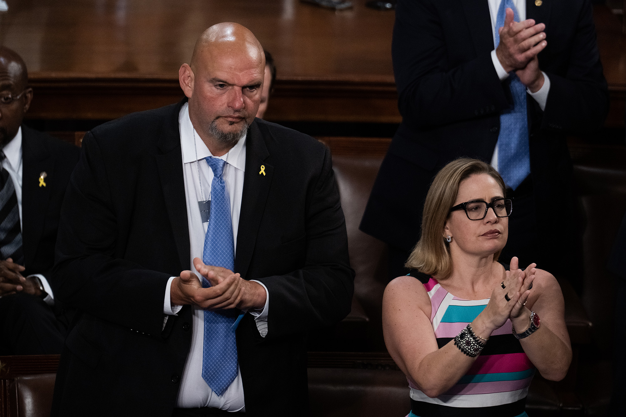 Senator John Fetterman in a suit and Senator Kyrsten Sinema clapping.