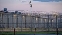 A large, windowless building behind a barbed wire fence.