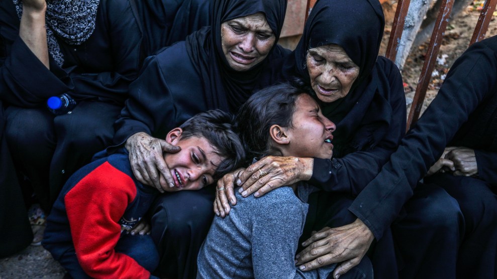 Two kneeling women in hijab comfort a young boy and girl who are crying.