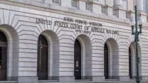 Front of a large gray-white brick court building with large exterior lettering reading "John Minor Wisdom United States Court of Appeals Building Fifth Circuit" above five arched doorways.