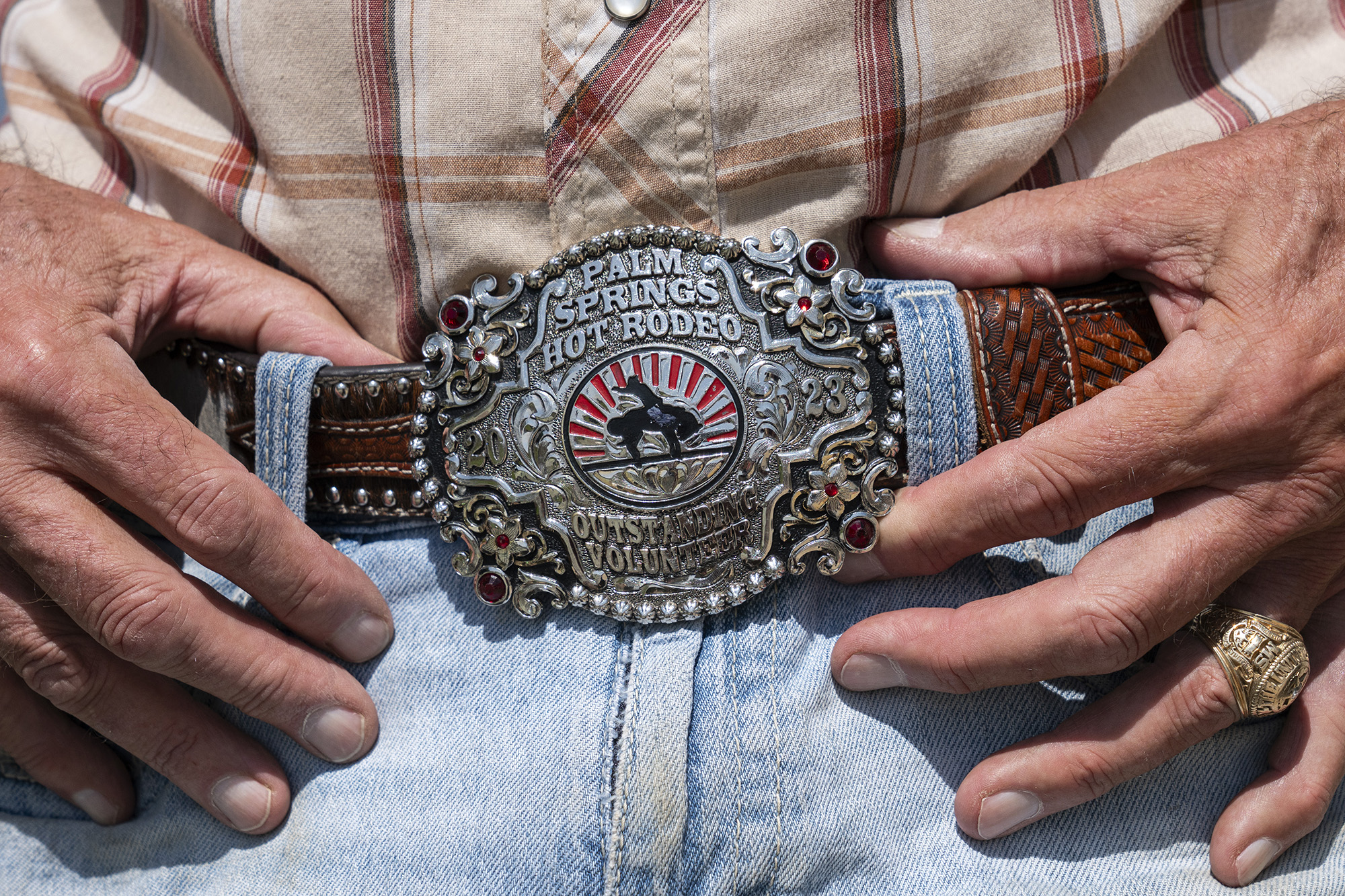 Close-up of a large silver belt buckle that reads, "Palm Springs Hot Rodeo." Red jewels are inset in the corners and the center has an enameled image of a cowboy riding a bucking animal.