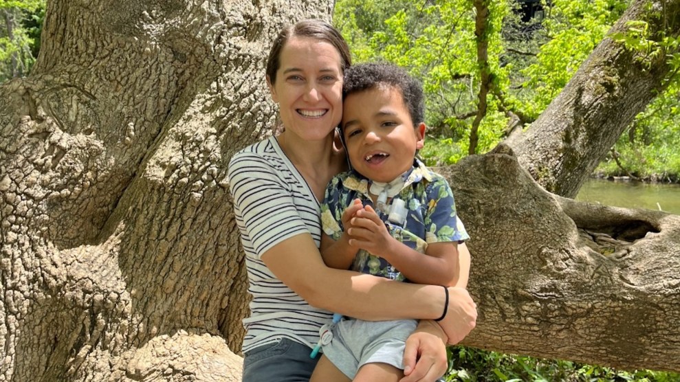 Beth Connor, a white woman, sitting on a tree branch holding her son, who has brown skin, in her lap.