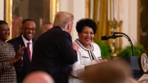 Alice Marie Johnson stands at a podium while Donald Trump talks to her.