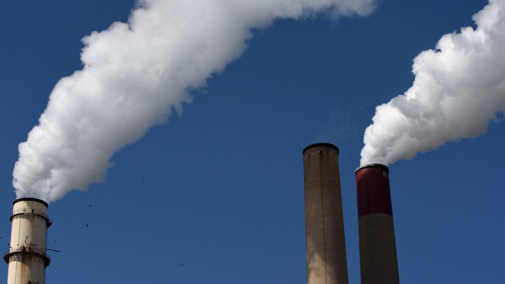 Close-up of the tops of three smokestacks, two with billowing white smoke against a bright blue sky.