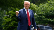 Donald Trump, in suit and tie while outdoors, yells in the direction of the camera while using his thumb to point at something over his right shoulder.
