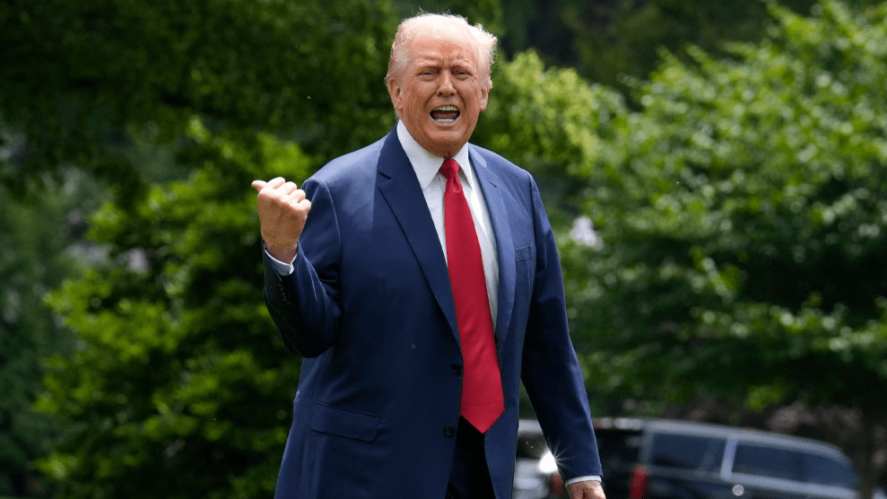 Donald Trump, in suit and tie while outdoors, yells in the direction of the camera while using his thumb to point at something over his right shoulder.