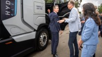 Closeup image of a Nikola Truck with the passenger door slightly ajar and Gov. Gavin Newsom in a suit standing in front of it alongside two other people.