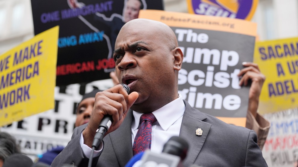 A man speaking into a microphone in front of protest signs.