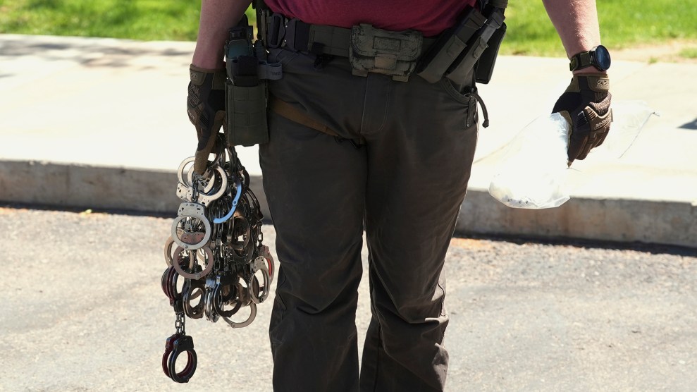 A uniformed officer pictured from the chest down holding many pairs of handcuffs.