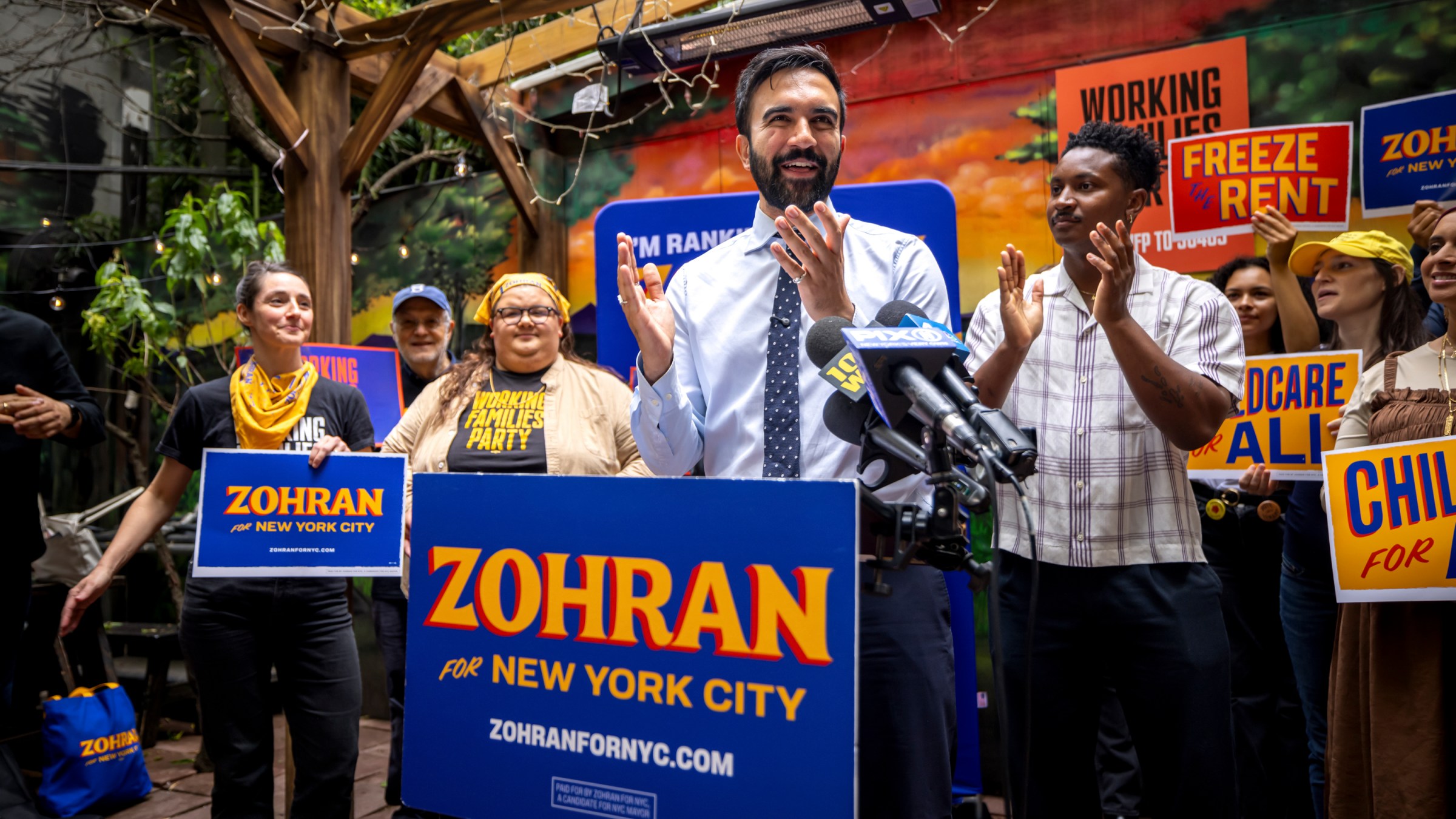 Zohran Mamdani speaks to a crowd of supporters, who hold campaign signs.