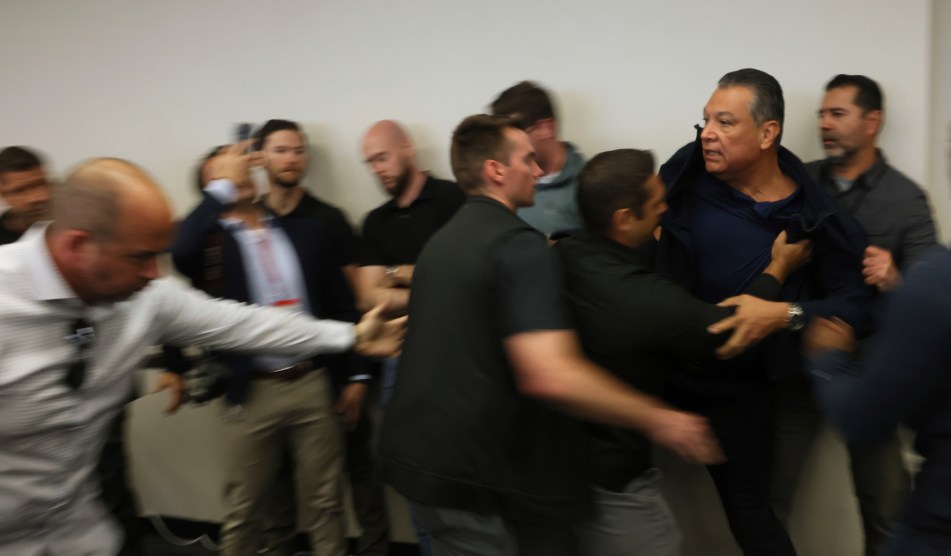 a blurry image with Padilla in focus being forced out of a DHS press conference
