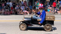 An image of a bedraggled Uncle Sam in an old jalopy duirng a July 4 parade.