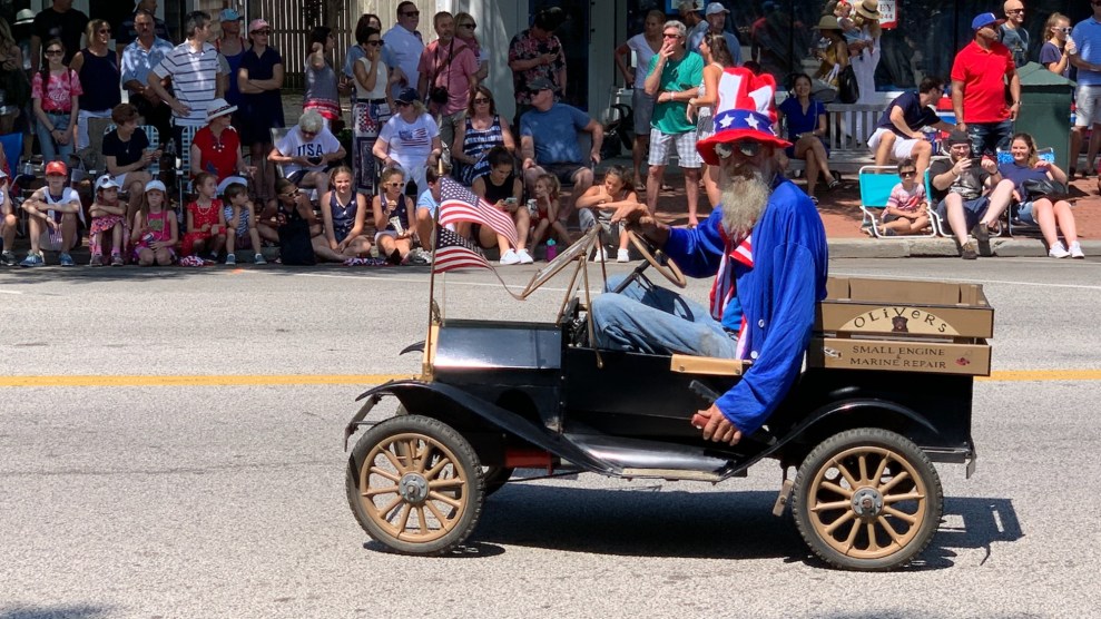 An image of a bedraggled Uncle Sam in an old jalopy duirng a July 4 parade.