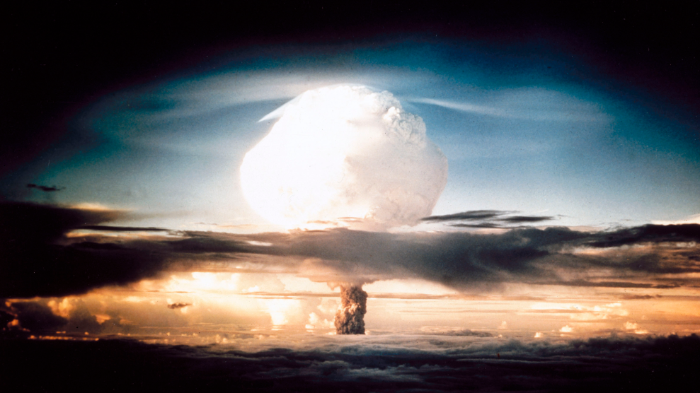 The white cap of a mushroom cloud billows outward from deep darkness in the upper sky. There are bright, fiery oranges and yellows closer to the horizon.