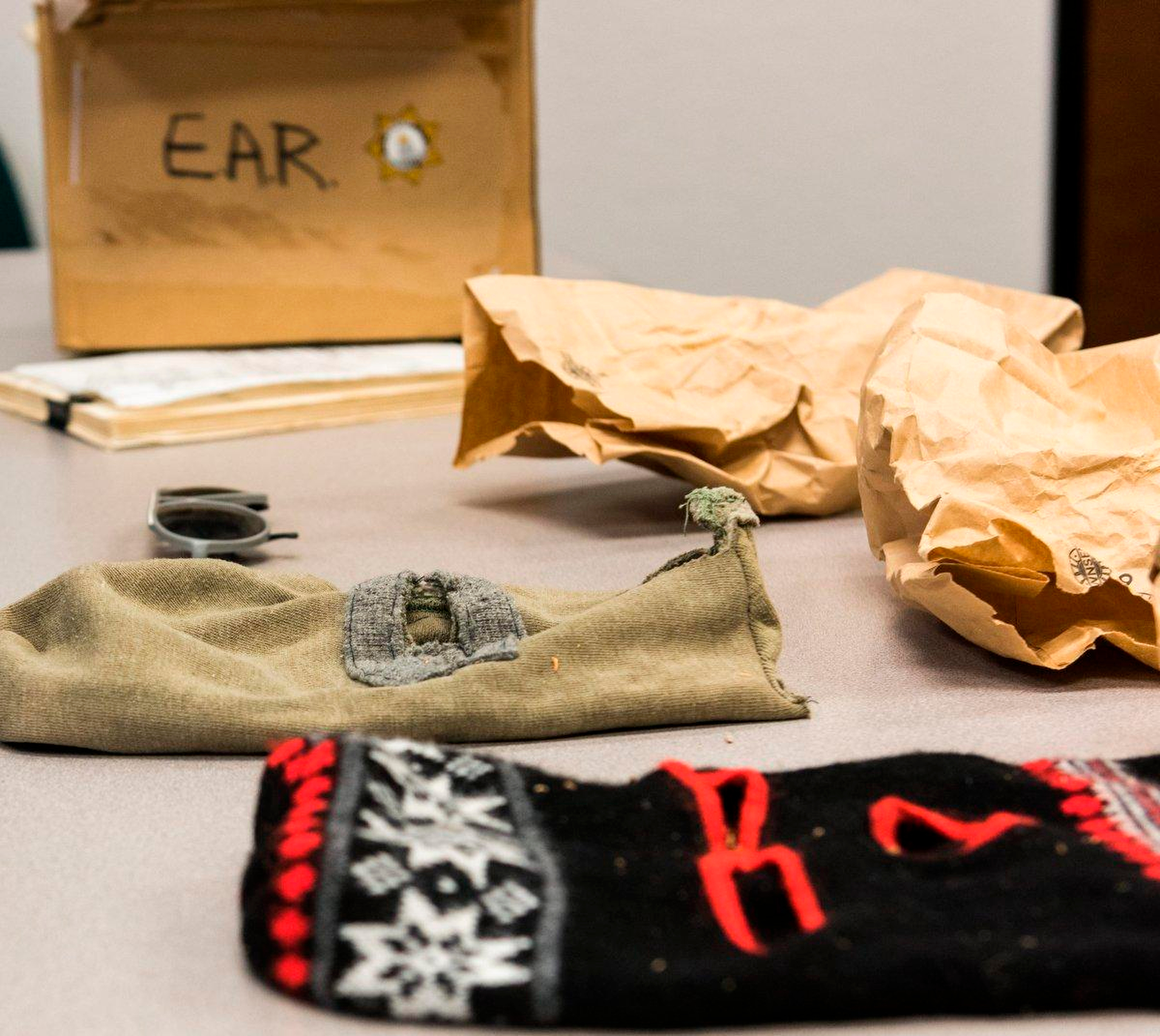 Two ski masks sit on a table near crumpled manila bags.