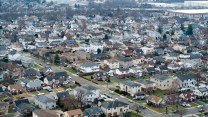 Aerial shot of a neighborhood of homes, trees with no leaves, and streets with parked cars.