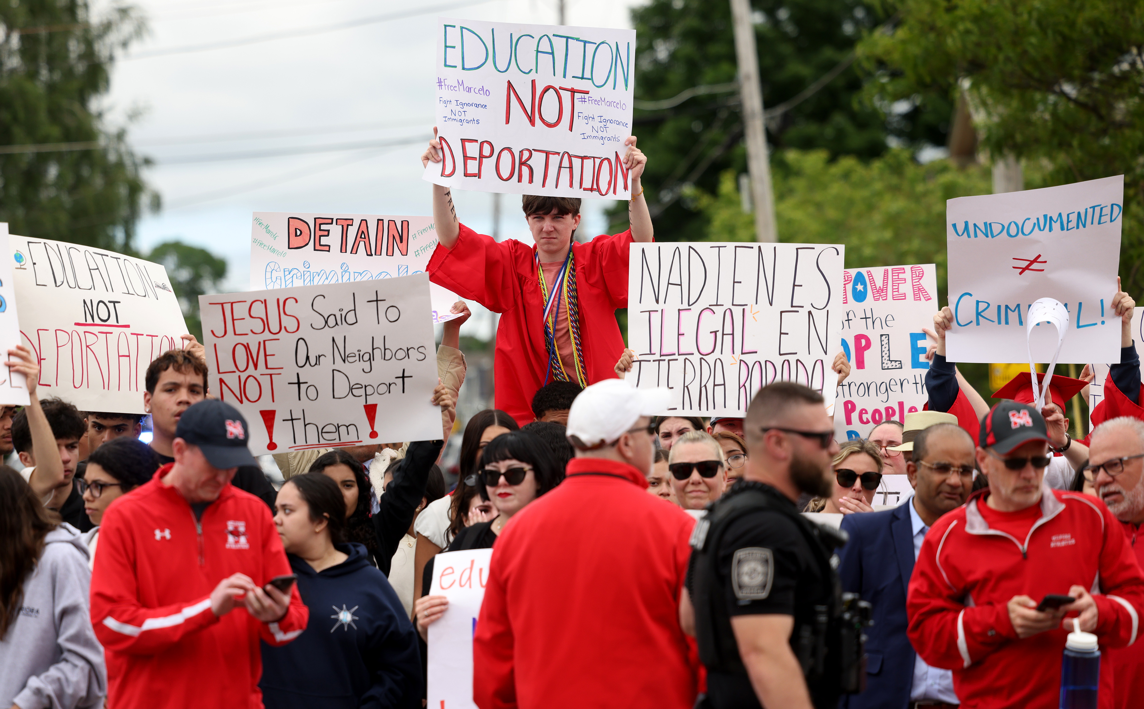A boy in a graduation gown on someones shoulders holding a protest sign that says"Education not deportation," Along with other students in gowns.