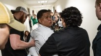 Two ICE agents escort a handcuffed man down a crowded hallway, after detaining him when he exited an immigration hearing.