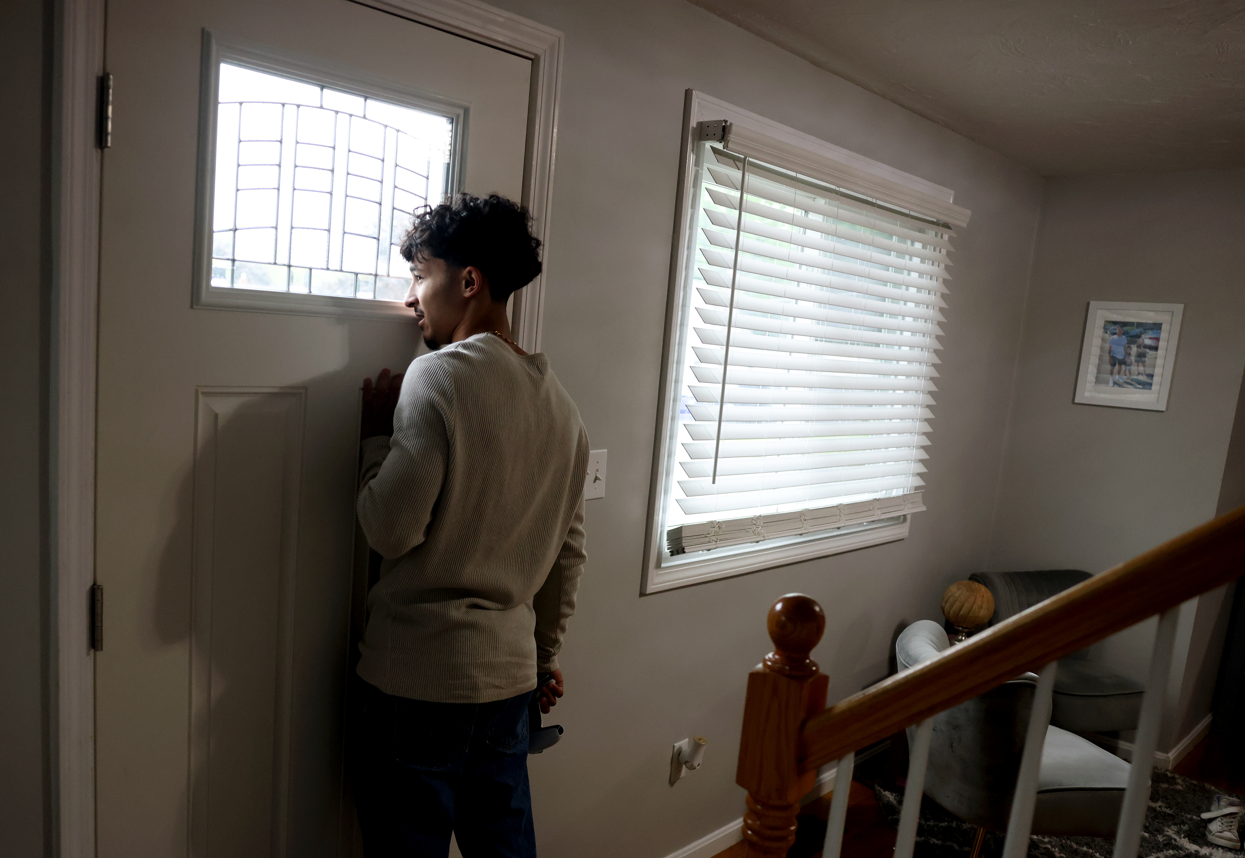 A boy is standing inside his home, looking outside the window of the front door.
