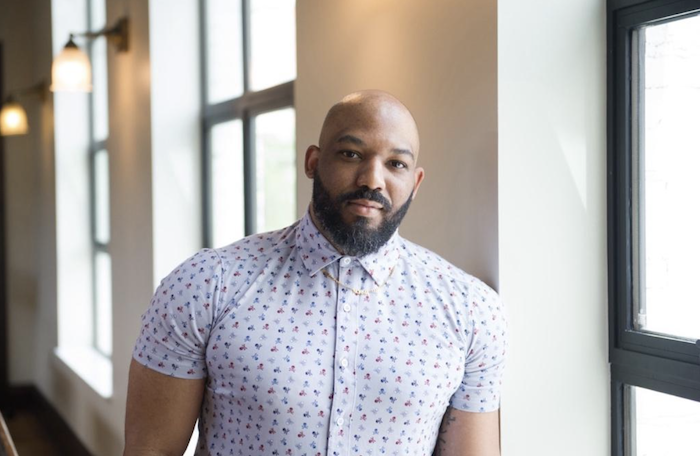 AJ Link, a black man with a beard in a blue patterned shirt, in a hallway