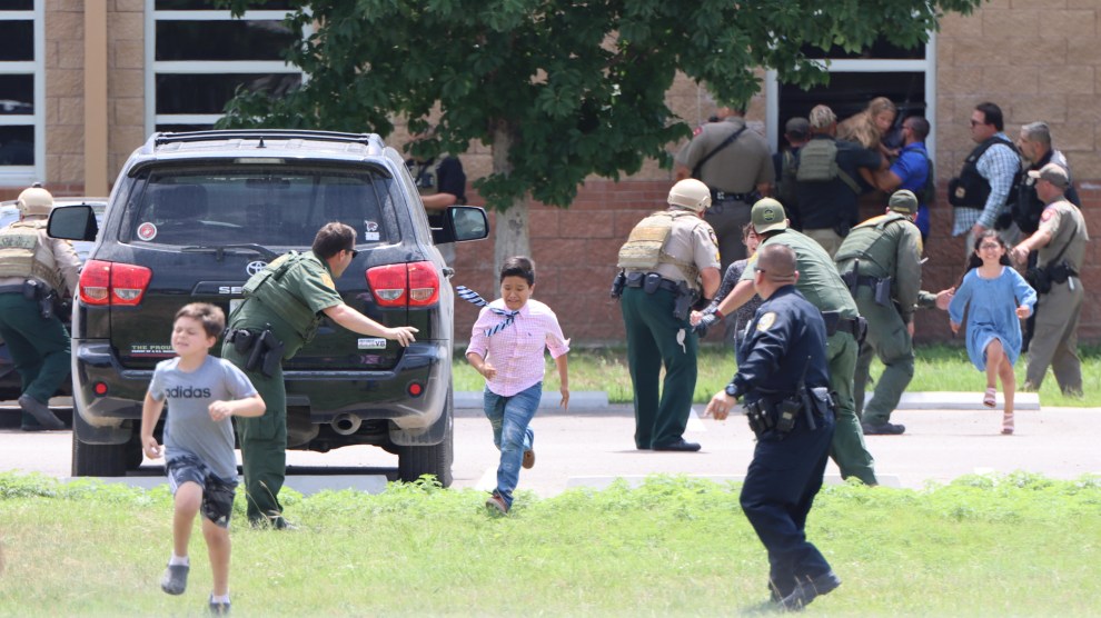 Three children run out of a school building. Several law enforcement officers in various uniforms stand outside, waving at the children to keep running.