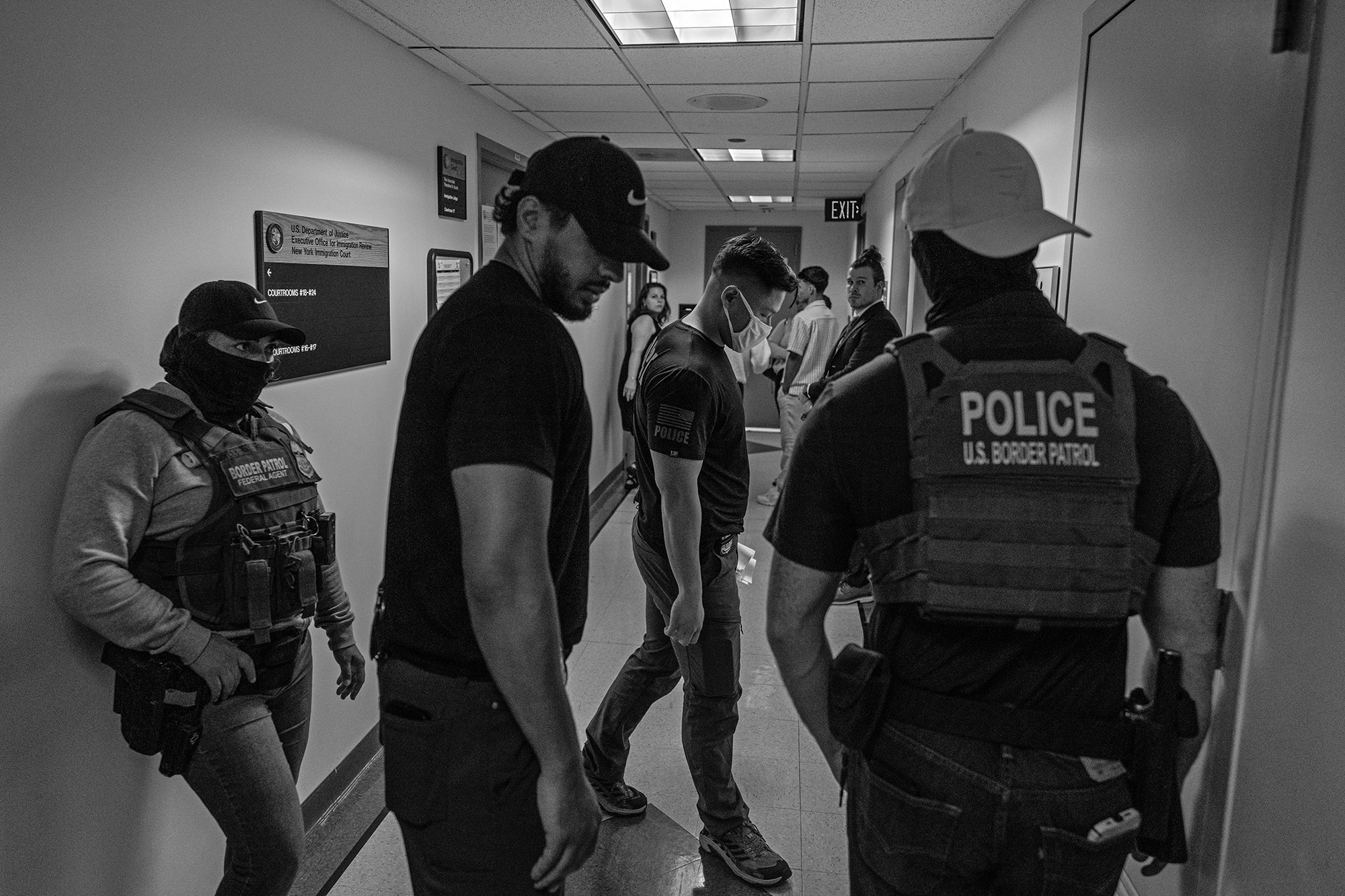 ICE agents and Border Patrol agents stand around a hallway.